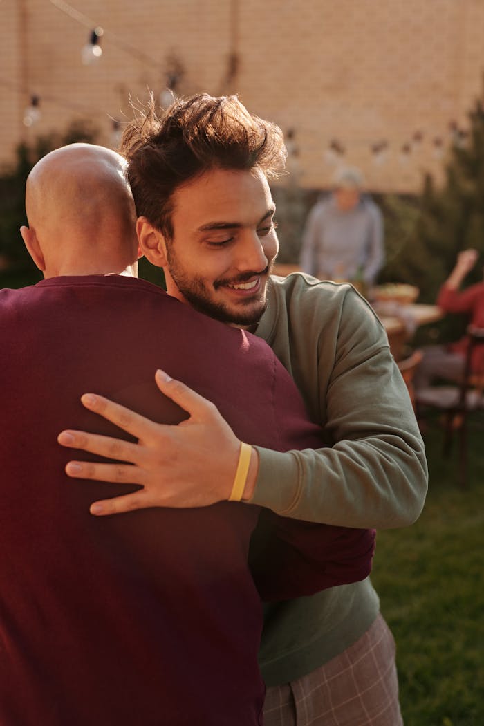 Two men hugging warmly in a sunny outdoor yard gathering.